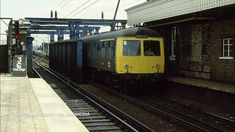 a yellow and black train traveling down tracks next to a brick covered station with an awning