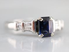 This is a classic style engagement ring, featuring bright baguette and round cut diamonds inlaid in each shoulder. The center gem is a high-quality blue Ceylon sapphire from Sri Lanka. This is a deeply colored stone with outstanding glitter, one of the finest in our collection. Metal: Platinum Gem: Ceylon Sapphire 1.59 Carats Gem Measurements: 5.4 x 7.3 mm, Emerald Cut Accents: 6 Diamonds totaling .30 Carats, G in Color, VS in Clarity Ring Size: 7.75 Marks: "@PT900FG" Stamped on the inside band Classic Sapphire Ring With Baguette Diamonds, Classic Style Engagement Rings, Platinum Sapphire Ring, Ceylon Sapphire Ring, Sapphire And Diamond Engagement Ring, Platinum Wedding Band, Ring Sapphire, Sapphire And Diamond Ring, Platinum Wedding