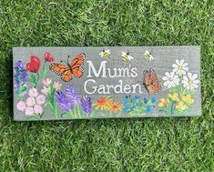 a sign that says mum's garden with butterflies and flowers on it in the grass