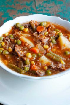 a white bowl filled with stew on top of a blue and green table cloth next to a spoon