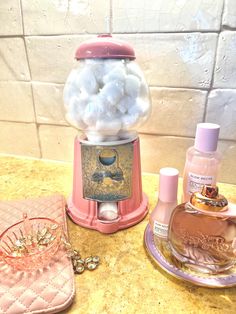 an assortment of perfumes on a counter next to a pink purse and bottle with bubbles in it