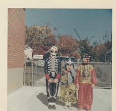 three people in skeleton costumes standing next to each other on a sidewalk near a fence