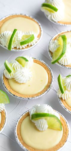 several small pies with lime slices and whipped cream on top are arranged in rows