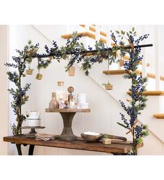 a wooden table topped with blue berries and greenery next to a bannister