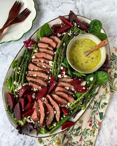 a plate with steak and asparagus on it next to a bowl of dressing