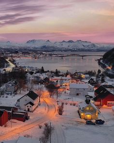 a small town is lit up at night in the snow with mountains in the background