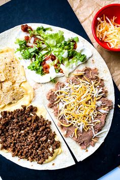 a tortilla topped with meat, cheese and other toppings next to a bowl of salad