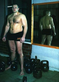 a man standing in front of a mirror with kettles on the ground next to him