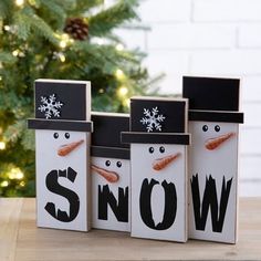 three snowmen are standing next to each other on a wooden table with a christmas tree in the background