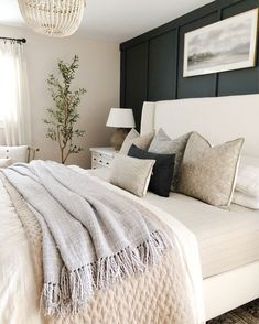 a white bed topped with lots of pillows next to a painting on the wall above it