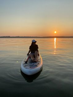 a man riding on top of a paddle boat in the middle of water at sunset