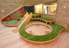 an indoor play area with artificial grass and wooden benches on the ground, in front of a wood paneled wall