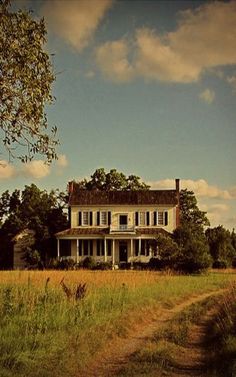 an old house sits in the middle of a field with tall grass and trees around it