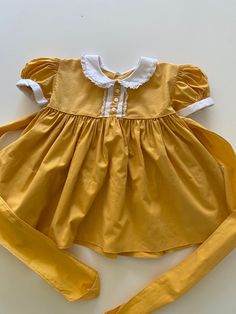 Vintage 1950's era little baby dress.  Golden yellow cotton with white sleeve cuffs, peter pan collar, decorative buttons and lace accents.  Full gathered skirt. Buttons and ties in the back.  Excellent vintage condition.   label:  none; looks to be handmade fabric:  cotton size:  none; size 6-9 months is just an estimate.  Please check measurements for an accurate fit.  Questions are welcome! dress was measured across the front side lying flat underarm to underarm 10 1/2" length 15" shoulder 9" Vintage Cotton Dress For Dress-up, Classic Cotton Dress With Lace Collar, Vintage Cotton Dress For Dress-up Occasions, Fitted Cotton Vintage Dress With Doll Collar, Yellow Puff Sleeve Cotton Dress, Yellow Cotton Puff Sleeve Dress, Yellow Cotton Retro Vintage Dress, Vintage Yellow Puff Sleeve Dress, Cotton Dress With Peter Pan Collar And Buttons