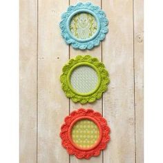 three frames with crocheted doily are hanging on a wooden wall, one is blue and the other is green