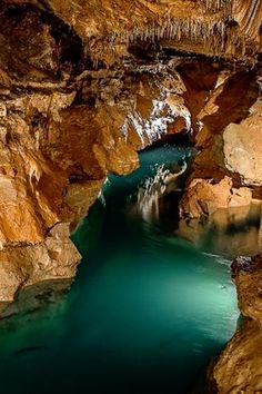 the water is blue and green in this cave with ice hanging from it's sides