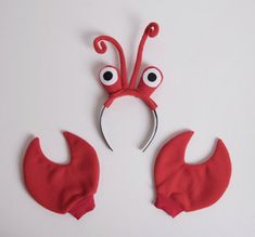 a pair of scissors with eyeballs attached to them on a white surface, next to two red mittens