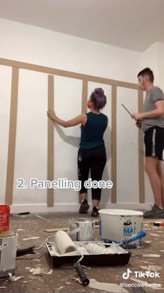 two people standing in an unfinished room with the walls torn down and one person holding a paint roller