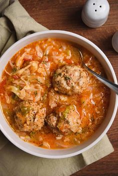 a white bowl filled with meatball soup on top of a wooden table next to a salt and pepper shaker