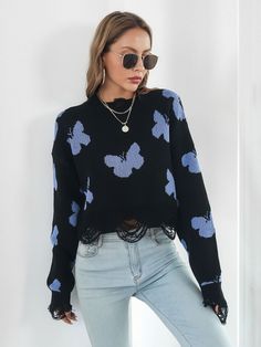 a woman wearing sunglasses and a black sweater with blue flowers on it is standing in front of a white wall