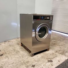 a silver washer sitting on top of a floor next to a garage door with roller shutters