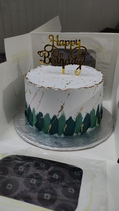 a white and green birthday cake sitting on top of a table next to a box