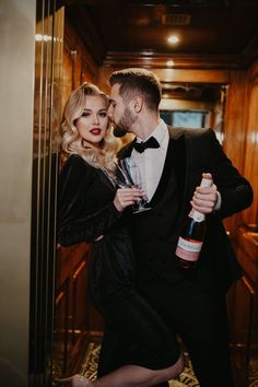 a man in a tuxedo kissing a woman with a bottle of wine on her shoulder