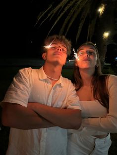 a man and woman standing next to each other in front of a palm tree at night