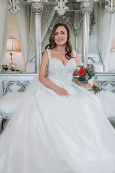 a woman in a white wedding dress sitting on a bed with roses and greenery