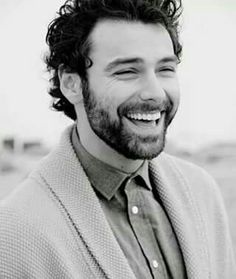 black and white photograph of a man with curly hair wearing a sweater smiling at the camera