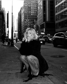 black and white photograph of woman sitting on curb talking on cell phone in new york city