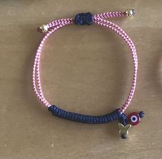 a pink and blue bracelet with an evil eye bead on the end is sitting on a table