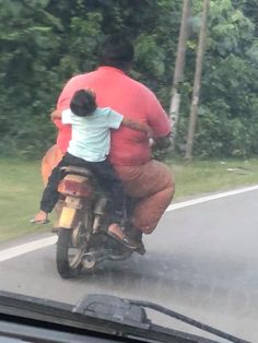 a man riding on the back of a motorcycle down a road with a child sitting on it