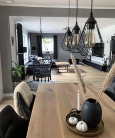 a wooden table topped with two black vases filled with white and brown flowers next to a living room