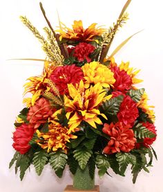 a vase filled with red and yellow flowers on top of a wooden table next to a white wall