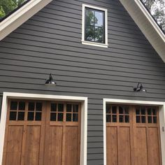 two brown garage doors in front of a gray house with white trim on the windows