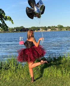 a woman in a tutu and dress is holding some balloons near the water's edge