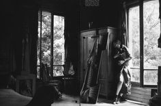 black and white photograph of a woman leaning against a cabinet in a room with large windows