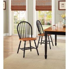 two wooden chairs sitting next to each other on top of a rug in front of windows