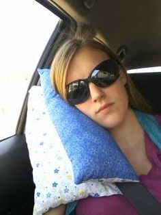 a woman sitting in the back seat of a car with her head resting on a pillow