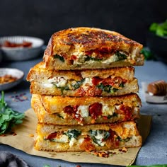 four slices of grilled cheese and tomato sandwich stacked on top of each other with basil leaves around the edges