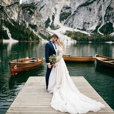 a bride and groom standing on a dock in front of boats