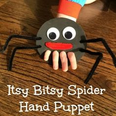 a hand holding a paper spider on top of a wooden table with the words, it's bitsy spider hand puppet