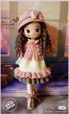 a crocheted doll wearing a pink hat and dress with long brown curly hair