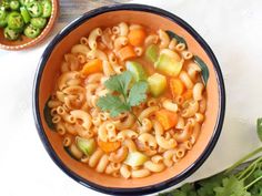 a bowl of pasta with carrots and celery on the side, next to a small bowl of broccoli