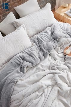 an unmade bed with white sheets and pillows on the floor next to a brick wall