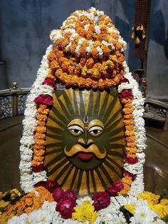 a statue with flowers around it and a sun face on the front, surrounded by other decorations