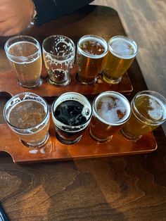 a wooden tray topped with lots of different types of beer glasses on top of a table