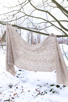 a white crocheted shawl hanging from a tree in the snow