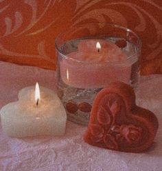 two heart shaped candles sitting on top of a bed next to a glass bowl filled with hearts